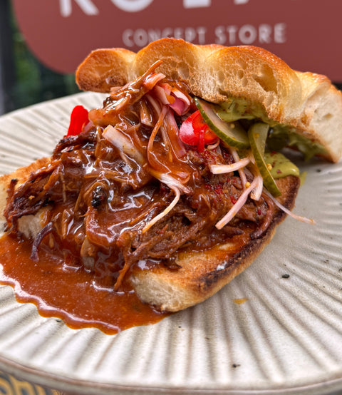 Sandwich with pulled meat and vegetables on a plate in front of a Kolab store sign.