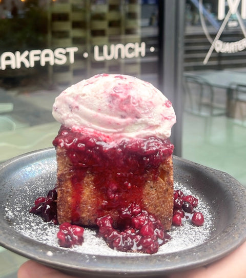 Dessert with ice cream and berry sauce on a plate, held in front of a restaurant entrance.