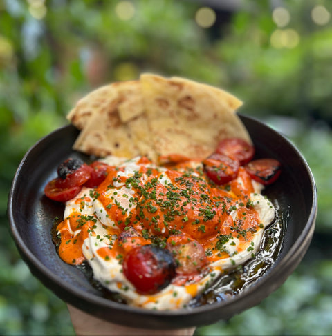 Platter of food with pita bread and roasted vegetables against a blurred green garden background